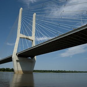 Underside of suspension bridge over a river under blue skies