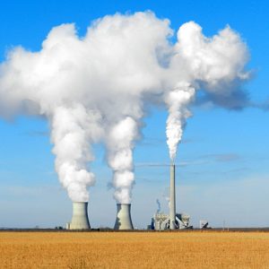 Power plant buildings emitting steam in field as see from far away