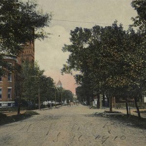 Trees and multistory brick building with tower on city street