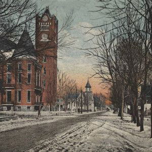 Multistory building with clock tower and multistory building with bell tower across from houses on town street in winter