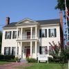 Multistory house with covered porch and balcony with sign and flagpole in the front yard