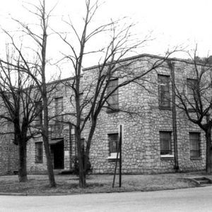 rectangular two-story stone building with small lawn bare trees sidewalk stop sign and street