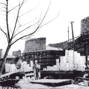 White woman standing outside in front of stacks of pottery and kilns