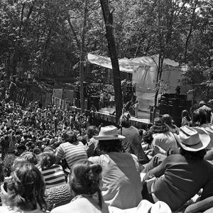 Crowd as seen from behind looking toward a stage with a white sheet-like covering