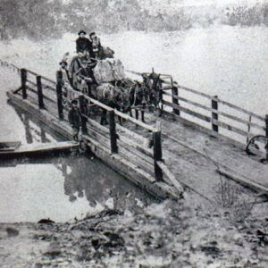 White couple on horse drawn wagon and white ferrymen landing ferry on river shore