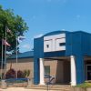 brick building with large blue entrance "OTC" and three flagpoles