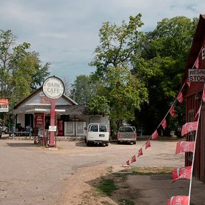 Storefront and cafe on dirt road with parked cars