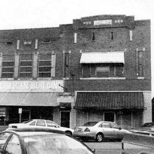 Parked cars on street outside multistory brick building with awnings over the sidewalk