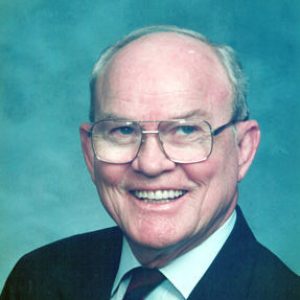 Old white man with glasses smiling in suit and tie