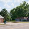 Single-story brick building with parking lot and abandoned wooden building on street with parking lot