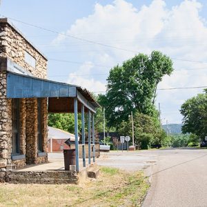 Stone store front with covered porch on street with various building in the background