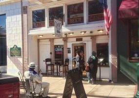 White women in coats talking outside restaurant with "Ohio Club" sign and Al Capone statue on bench