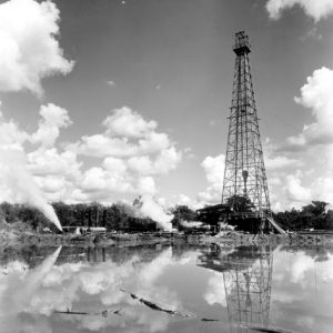 Oil derrick tower near body of water with sky reflected in the water