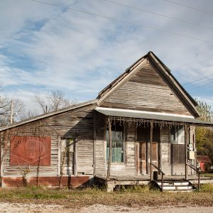 Abandoned building with covered porch and wood siding on grass