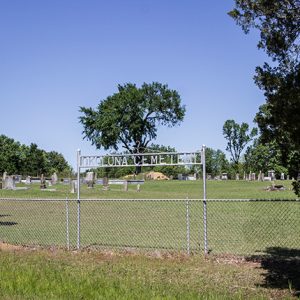 Fenced-in cemetery with iron "Okolona Cemetery" sign inside it