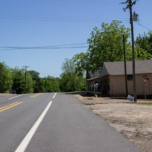 Single-story brick stores and garage building on two-lane road