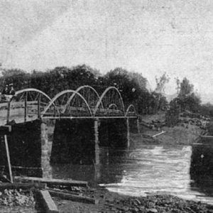 Horse drawn carriage crossing steel arch wooden bridge over river