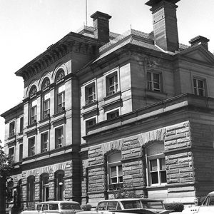 Multistory building with arched windows on street with parked cars in front of it