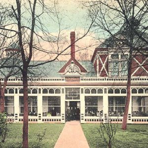 Brick building with large front windows and people sitting inside and a slender chimney and trees