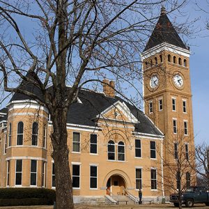 Multistory brick building with clock tower and bare trees in the foreground