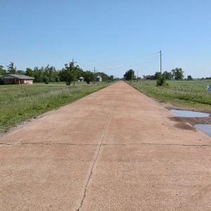 Cracked rural highway with single-story house and silos in the distance