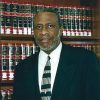 African-American man with graying beard in suit and tie standing at bookshelf