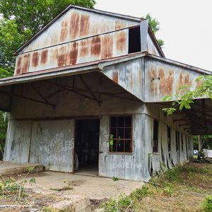 Abandoned rusting multistory gin building with covered entrance and walkway