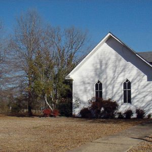 Single-story white church with steeple in autumn with sidewalk and sign