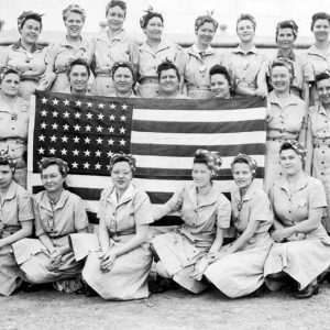 White women in uniform wearing bandanas pose with an American flag