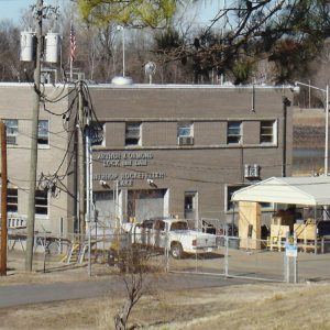 Two-story building next to river with parking lot and electrical poles