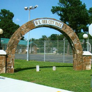 Stone arch entrance at park with basketball court and building with rock walls and street lights