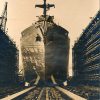 Large ship leaving dry dock with flag banner draped on its bow