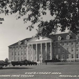 Multistory building with columns with cars parked in front and flagpole to the left