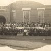 Assemblage of white people in front of brick building