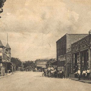 Looking down town street with people standing outside brick storefronts on both sides