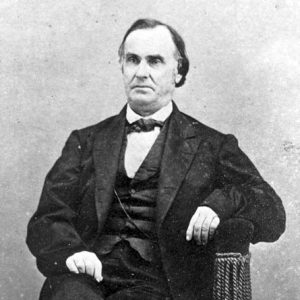 White man in a suit and tie sitting in a chair