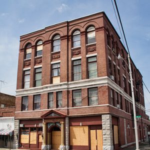 Four-story brick building on street corner with first floor windows papered over