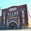 Multistory theater building with arched entrance behind chain link fence on street