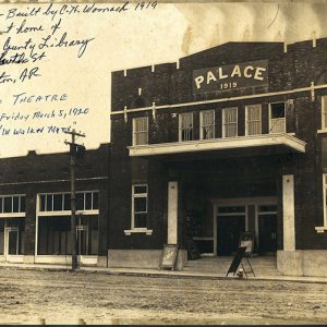 Multistory brick "Palace" theater and single-story buildings on street with handwritten notes