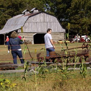 White crowd visiting farmstead with barn and machinery in field