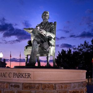 Statue of white man sitting in chair with open book on round base