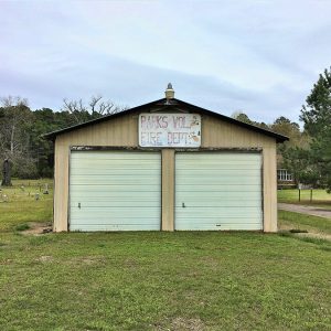 Metal two-car garage building with sign and cemetery on left side