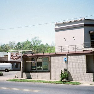 "We care budget inn" hanging sign on motel building on street with parking lot and white van