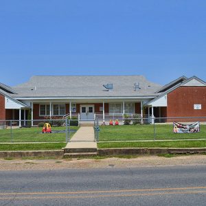 Single-story brick school building with two wings and pavilion in fenced in yard