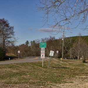 Highway curve section with road signs on both sides including green "Perry" sign