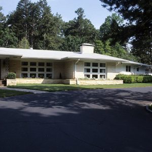 Single-story house with red and white door and banks of rectangular windows