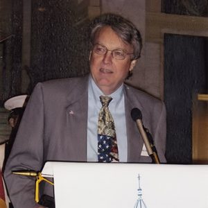 White man with glasses in suit speaking at lectern