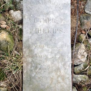 Stone grave marker on the ground with rocks and grass