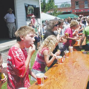 White children eating pickles with table and white crowd around them