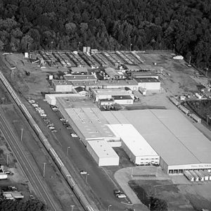 Train running on tracks in between warehouse buildings and two-lane residential street as seen from above